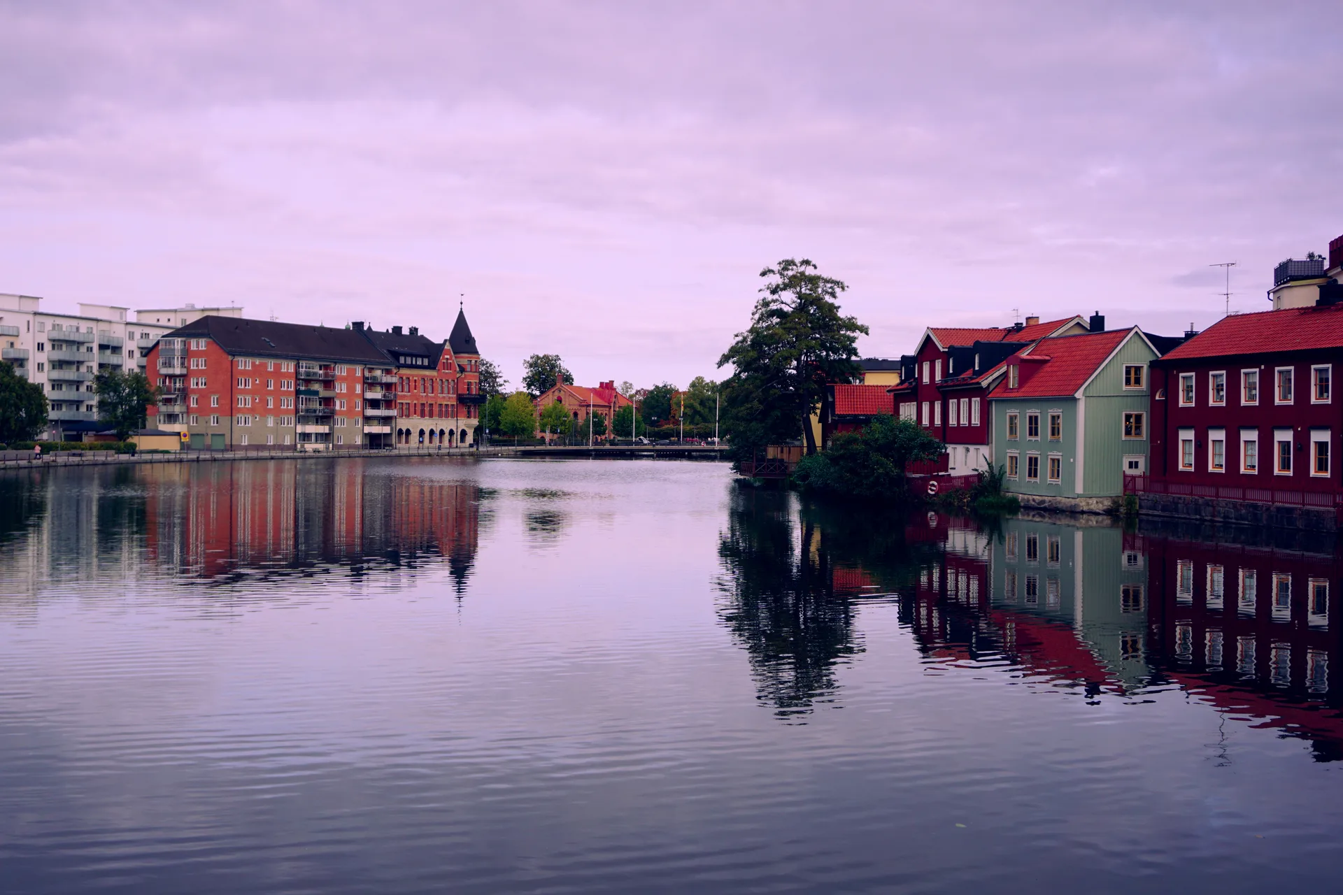 Lila skymningshimmel över ån i Eskilstuna, med flerbostadshus på ena stranden och äldre trähusbebyggelse på den andra